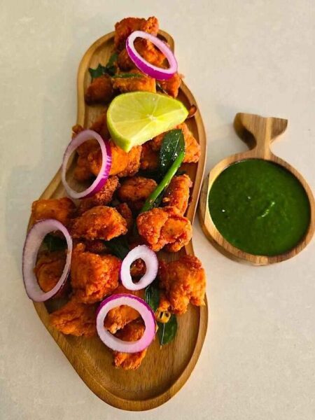 Delicious Chicken 65 arranged on a platter with lemon wedges and fresh green chutney.