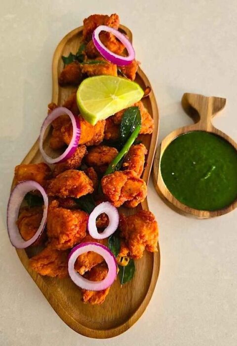 Delicious Chicken 65 arranged on a platter with lemon wedges and fresh green chutney.