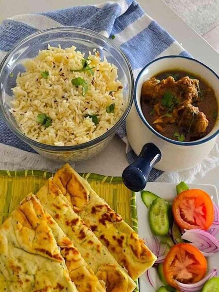 A platter featuring chicken curry, naan, rice, and fresh salads for a complete meal.