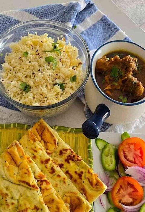 A platter featuring chicken curry, naan, rice, and fresh salads for a complete meal.