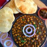 Chole Bhature platter with spicy chickpea curry, fluffy bhature, onions, and pickle.