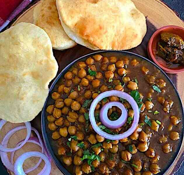 Chole Bhature platter with spicy chickpea curry, fluffy bhature, onions, and pickle.