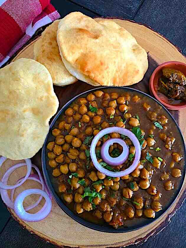 Chole Bhature platter with spicy chickpea curry, fluffy bhature, onions, and pickle.